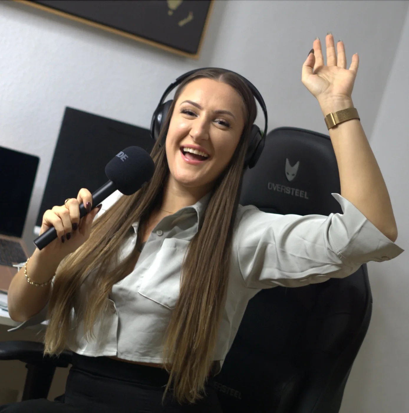 Elsinora in headphones with a microphone in one hand and the other hand raised